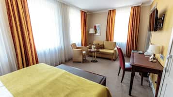 A hotel room with a bed, a sofa, a desk with a chair, and a small table.
