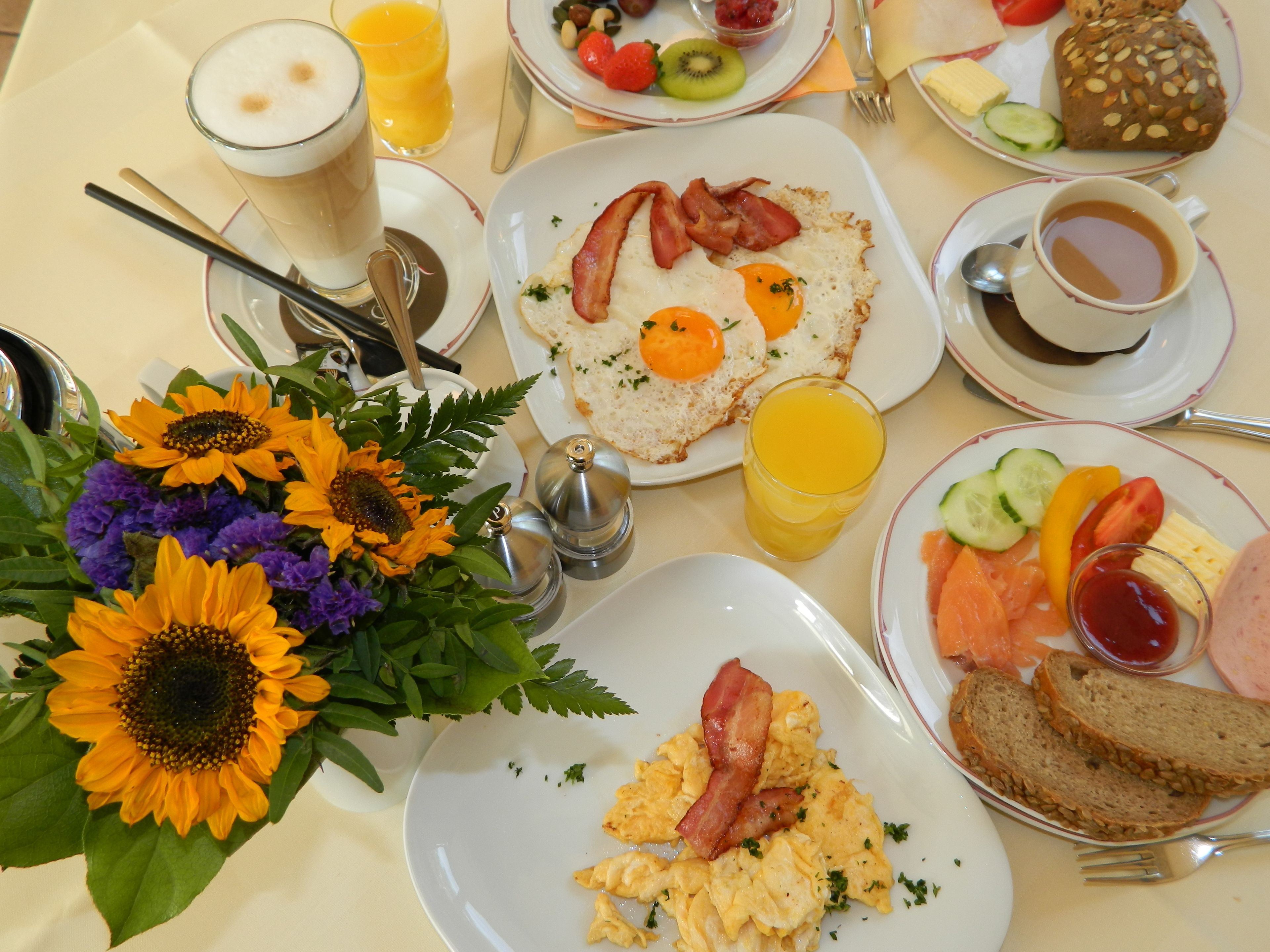 A breakfast setting with plates of eggs, bacon, toast, and fruit.