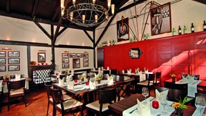 Un restaurante con mesas y sillas de madera, un muro rojo decorativo y una araña.