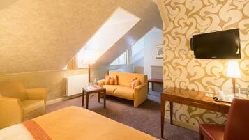 A hotel room with a bed, a sofa, a desk, and a TV.