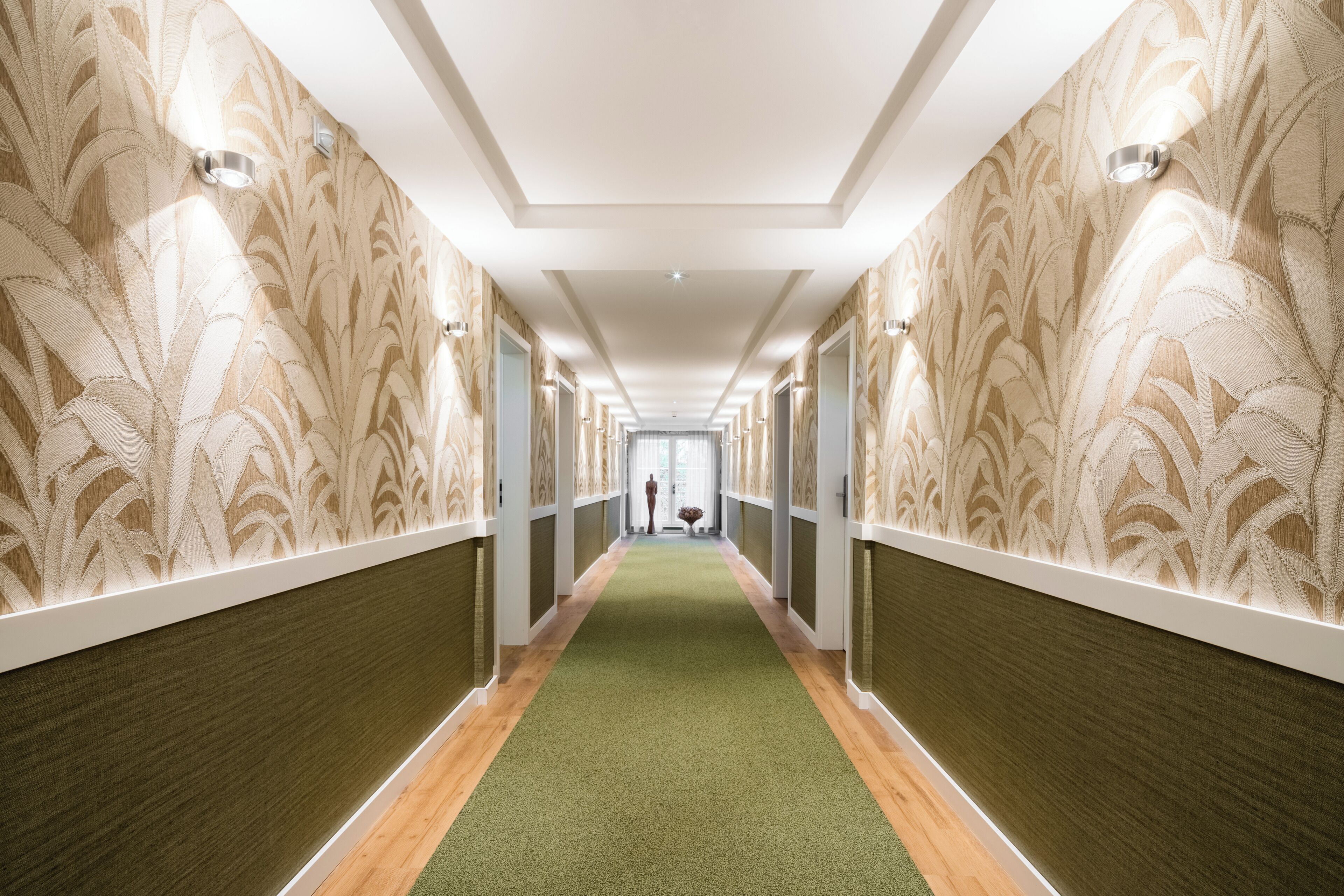 A hallway with patterned wallpaper, a green carpet, and a wooden floor.