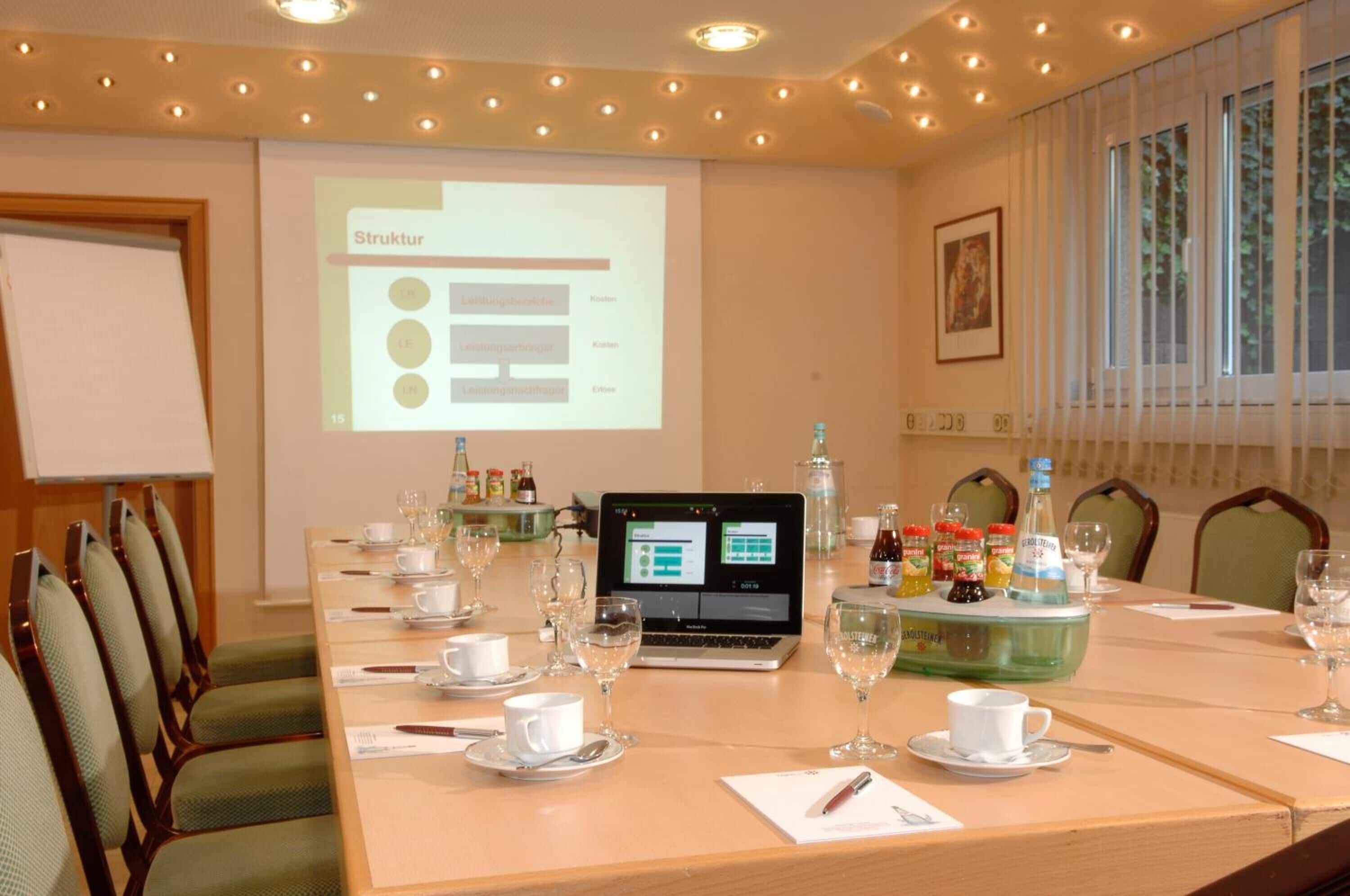 A conference room with a long table set for a meeting, a laptop, and a projector displaying a slide titled "Struktur".