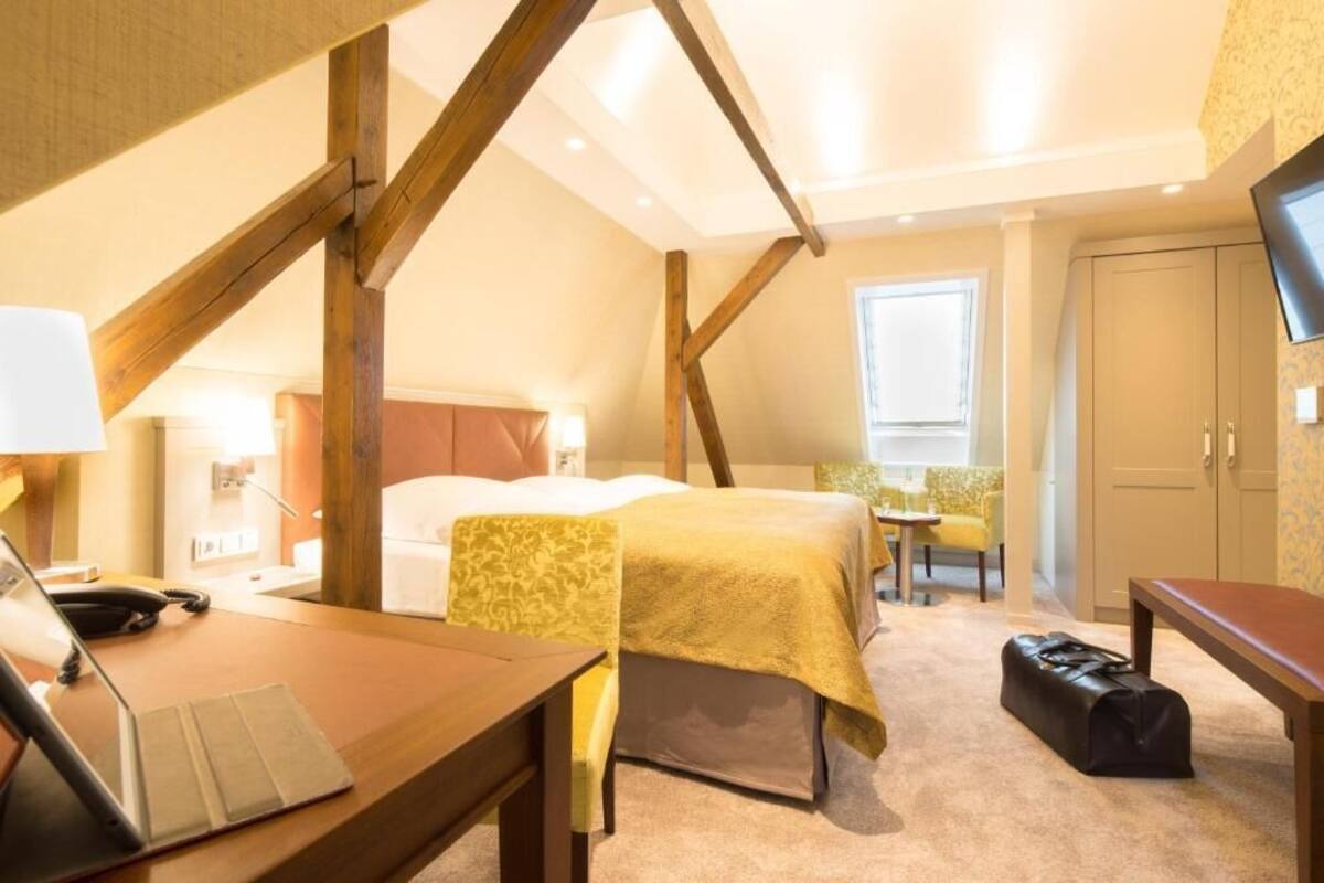 Una habitación de hotel con una cama, un escritorio con una computadora portátil, una maleta y un televisor en la pared.