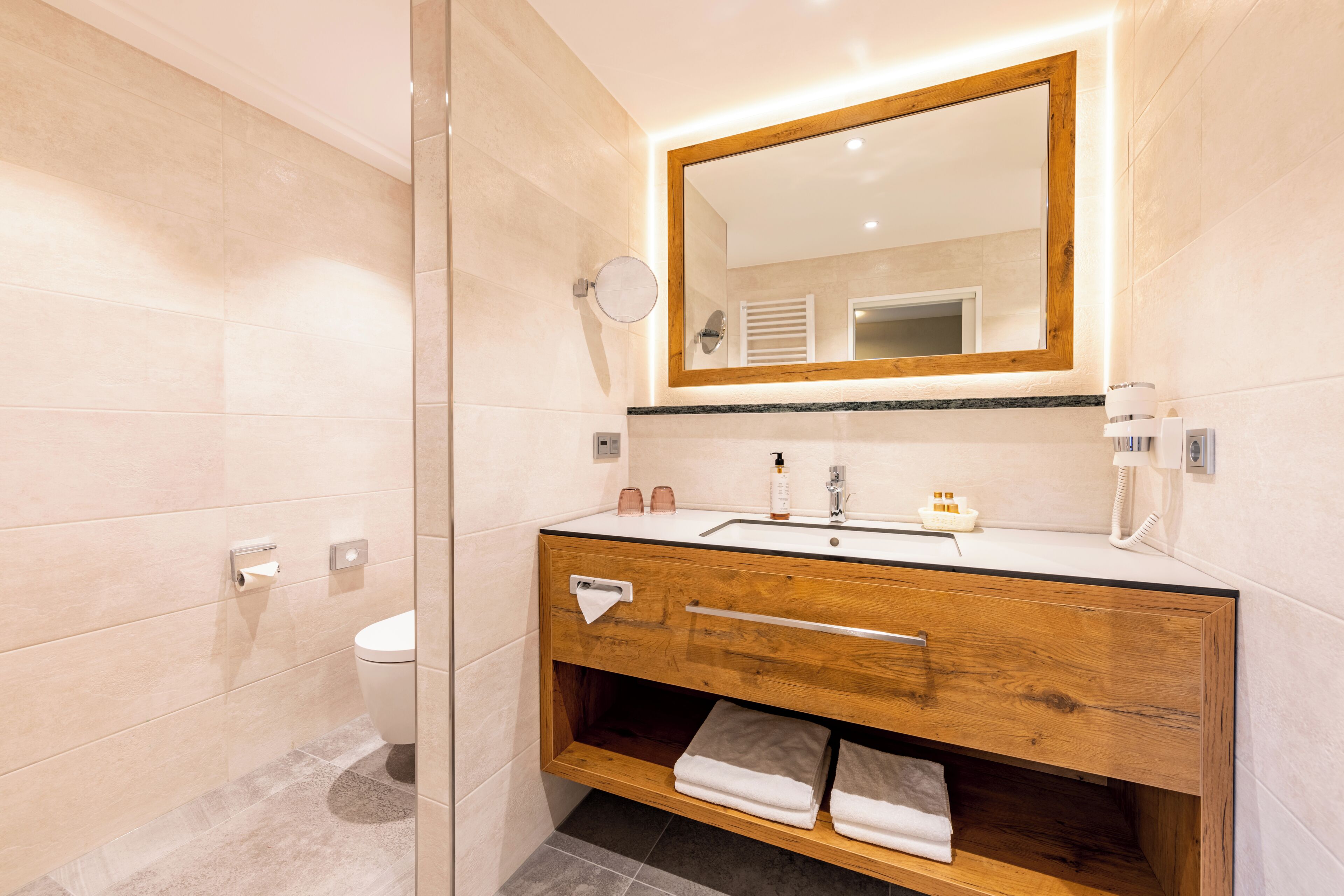 Un baño moderno con tocador de madera, un espejo grande y cabina de ducha con mampara de vidrio.