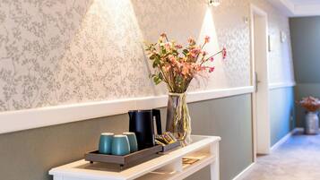 A hallway with a floral wallpaper, a vase with flowers, and a tray with cups and a book on a console table.