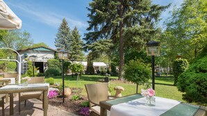 Un patio al aire libre con mobiliario de mimbre, una mesa con un jarrón de flores y vistas a un edificio con un letrero que dice "Schulhaus".