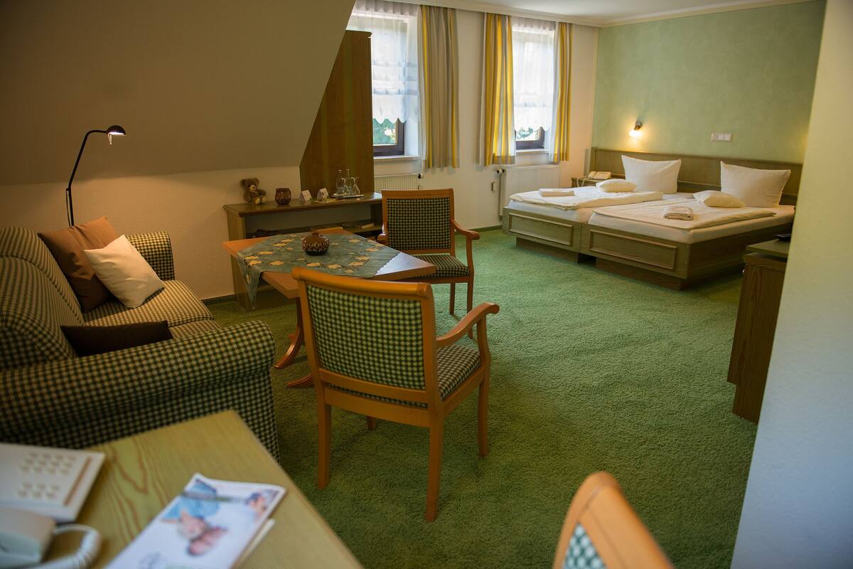 A hotel room with a checkered sofa, a dining table with chairs, a bed with two pillows, and a lamp.