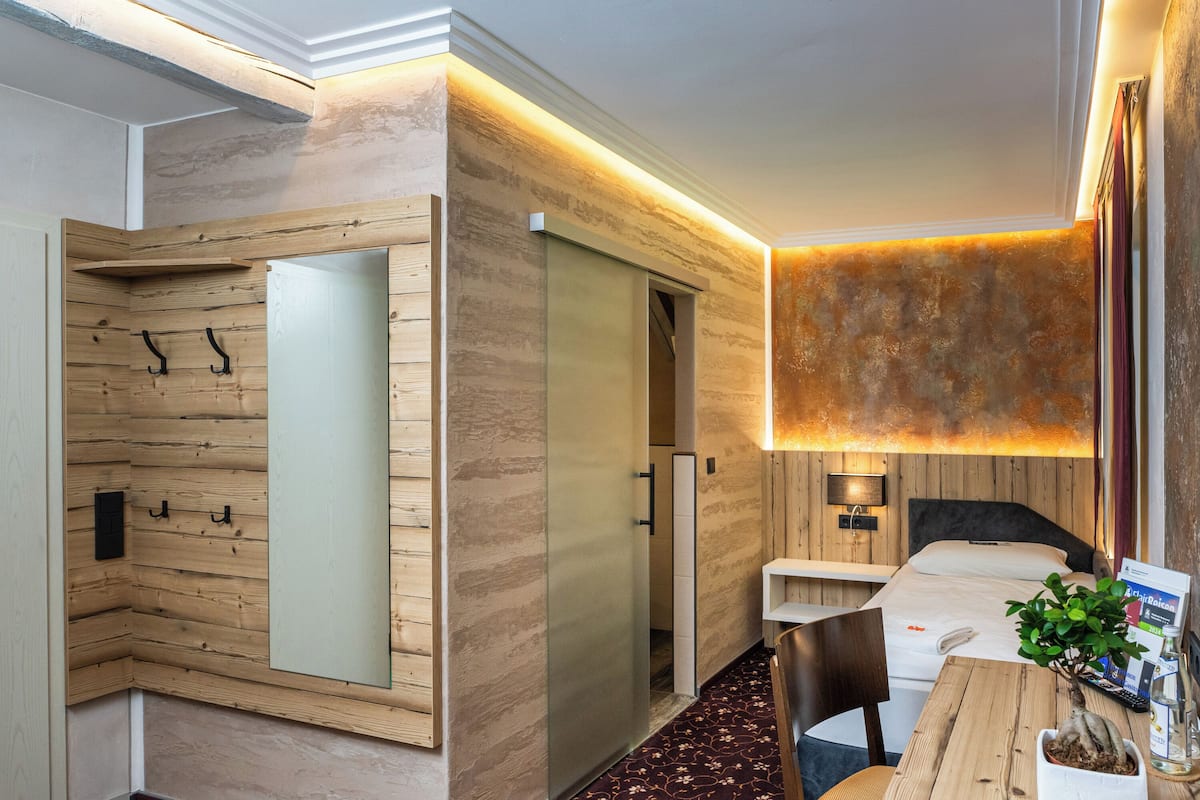 A hotel room with a wooden wall, a bed, a desk, and a chair.