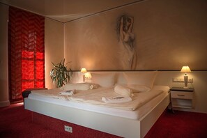 Un dormitorio con una cama grande, dos mesitas de noche con lámparas, una cortina roja y un cuadro en la pared.