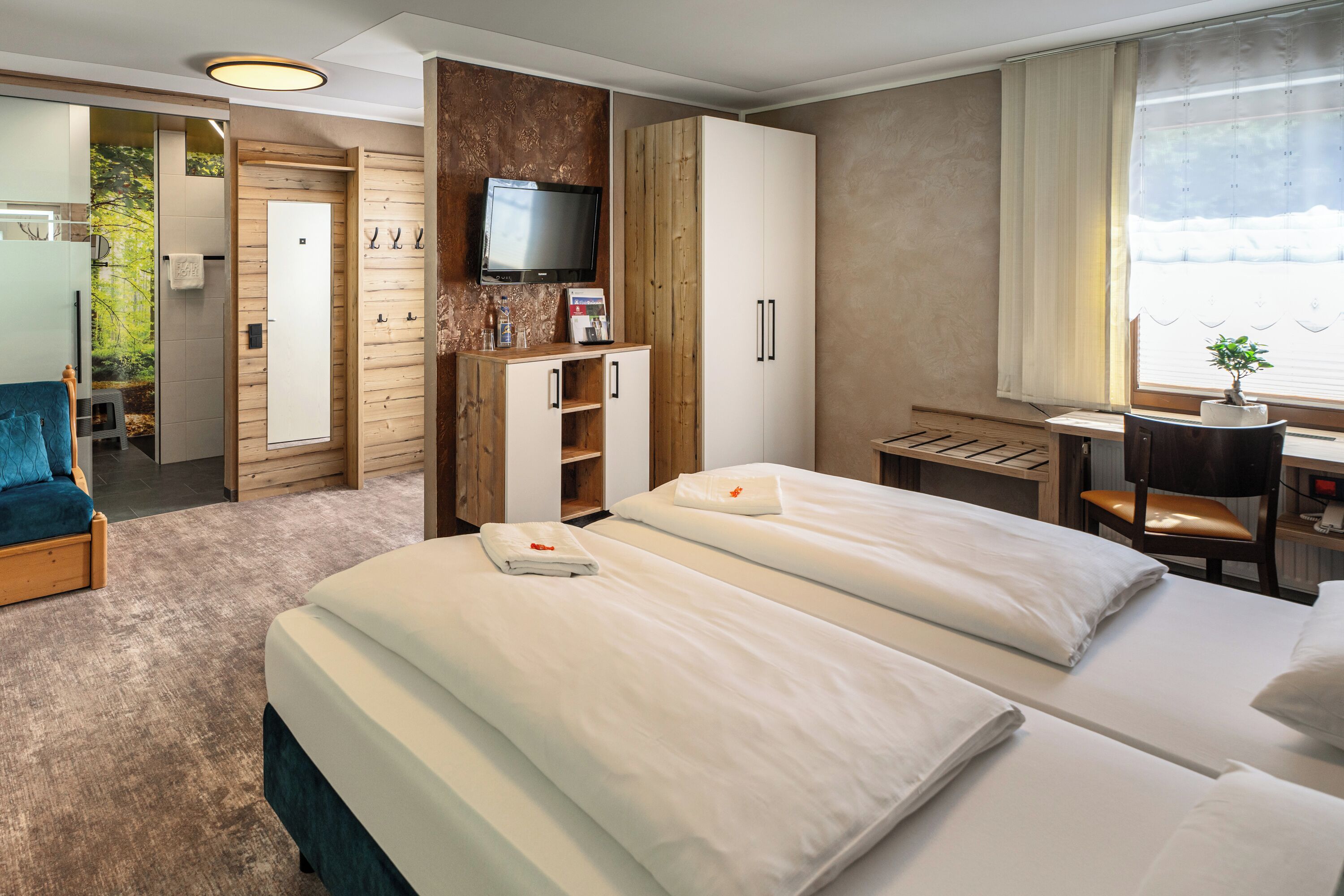 A hotel room with two beds, a desk, a TV, and a view of the outdoors.
