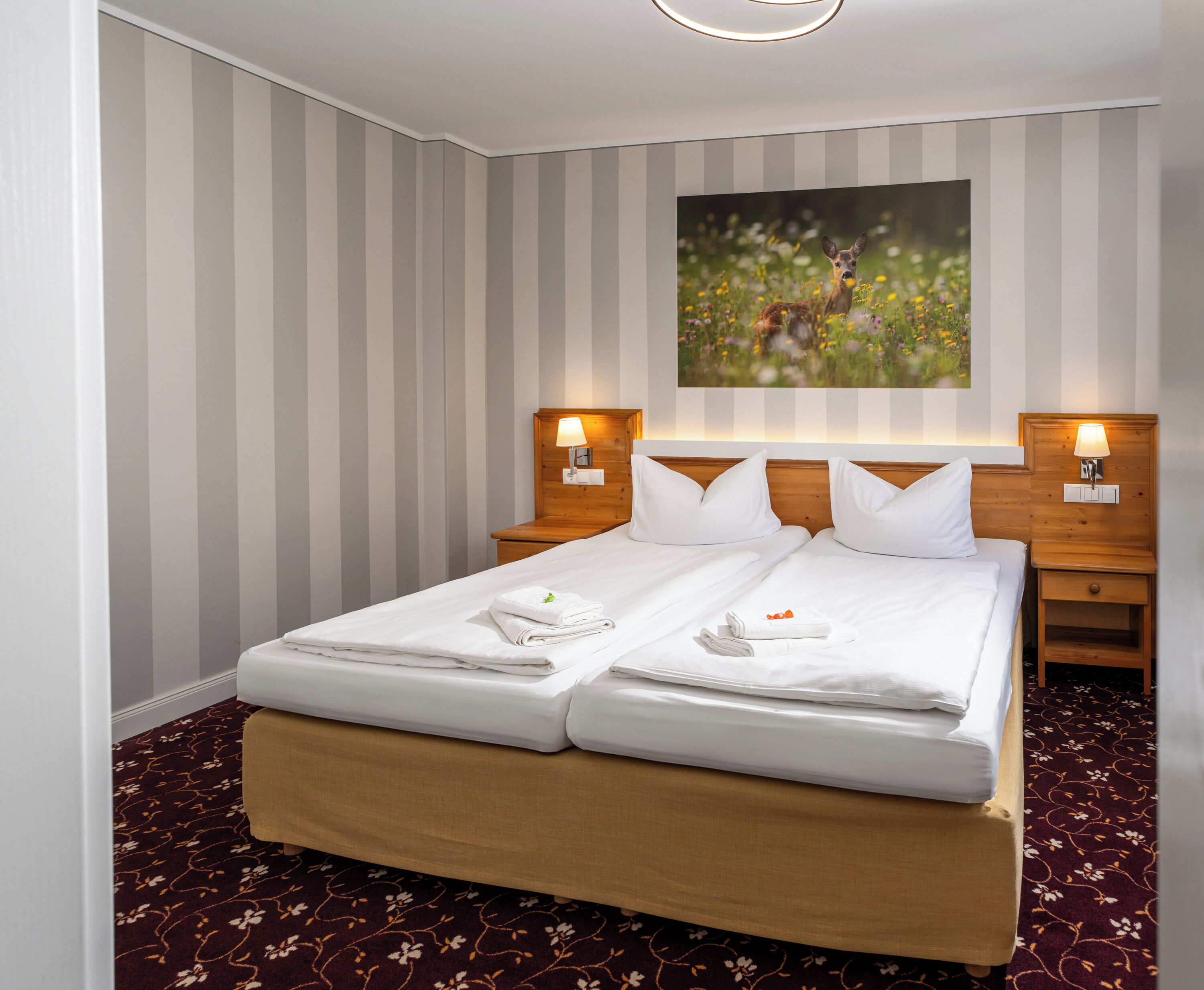 A hotel room with a double bed, two bedside tables, a headboard with a painting, and a striped wall.