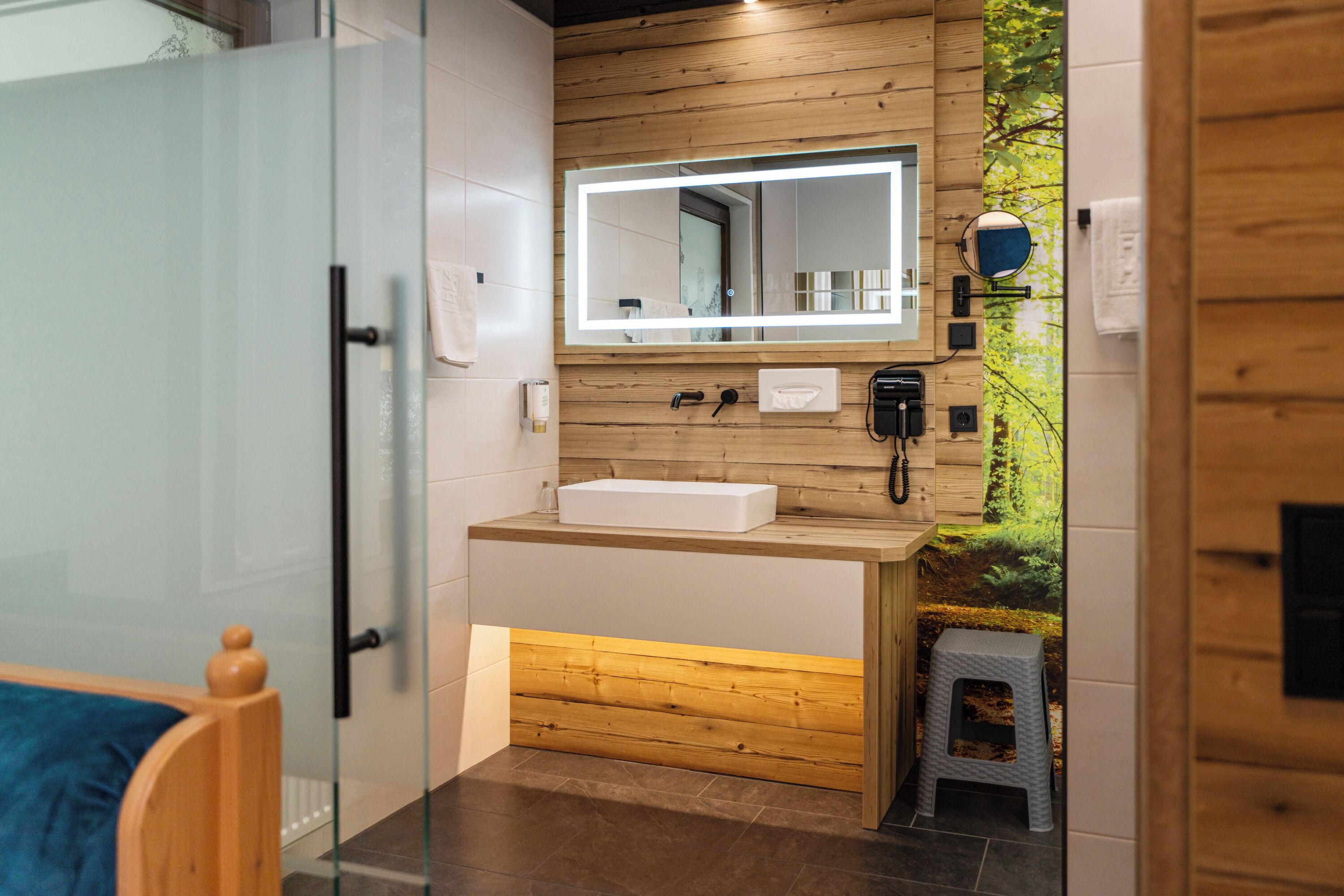 A modern bathroom with a wooden vanity, a large mirror, and a small stool.