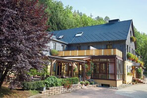 A two-story building with a balcony, a covered patio area, and a brick pathway leading to the entrance. - Flair Hotel Mellestollen (Saalfeld-Saale)
