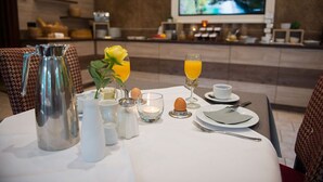 A dining table set with a pitcher, salt and pepper shakers, a candle, a flower arrangement, a glass of orange juice, a cup, and plates with cutlery. - Flair Hotel Mellestollen (Saalfeld-Saale)