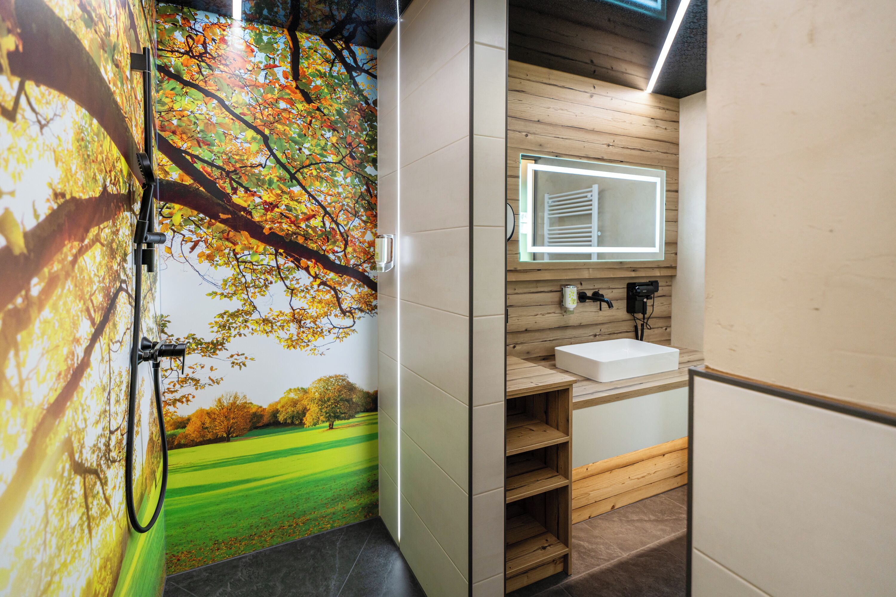A bathroom with a wooden wall, a white sink, a mirror, and a shower with a tree mural.