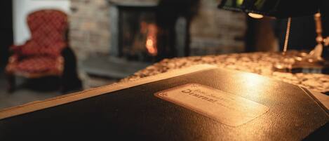 A leather-bound book with a label on a table in a warmly lit room with a brick wall and a fireplace.