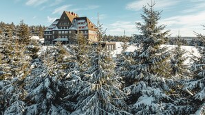 A large hotel with multiple floors and a prominent roofline, surrounded by snow-covered trees and a clear sky.