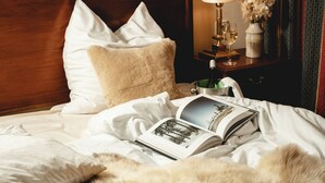 A neatly made bed with a book, pillows, a lamp, and a vase with flowers on a nightstand.