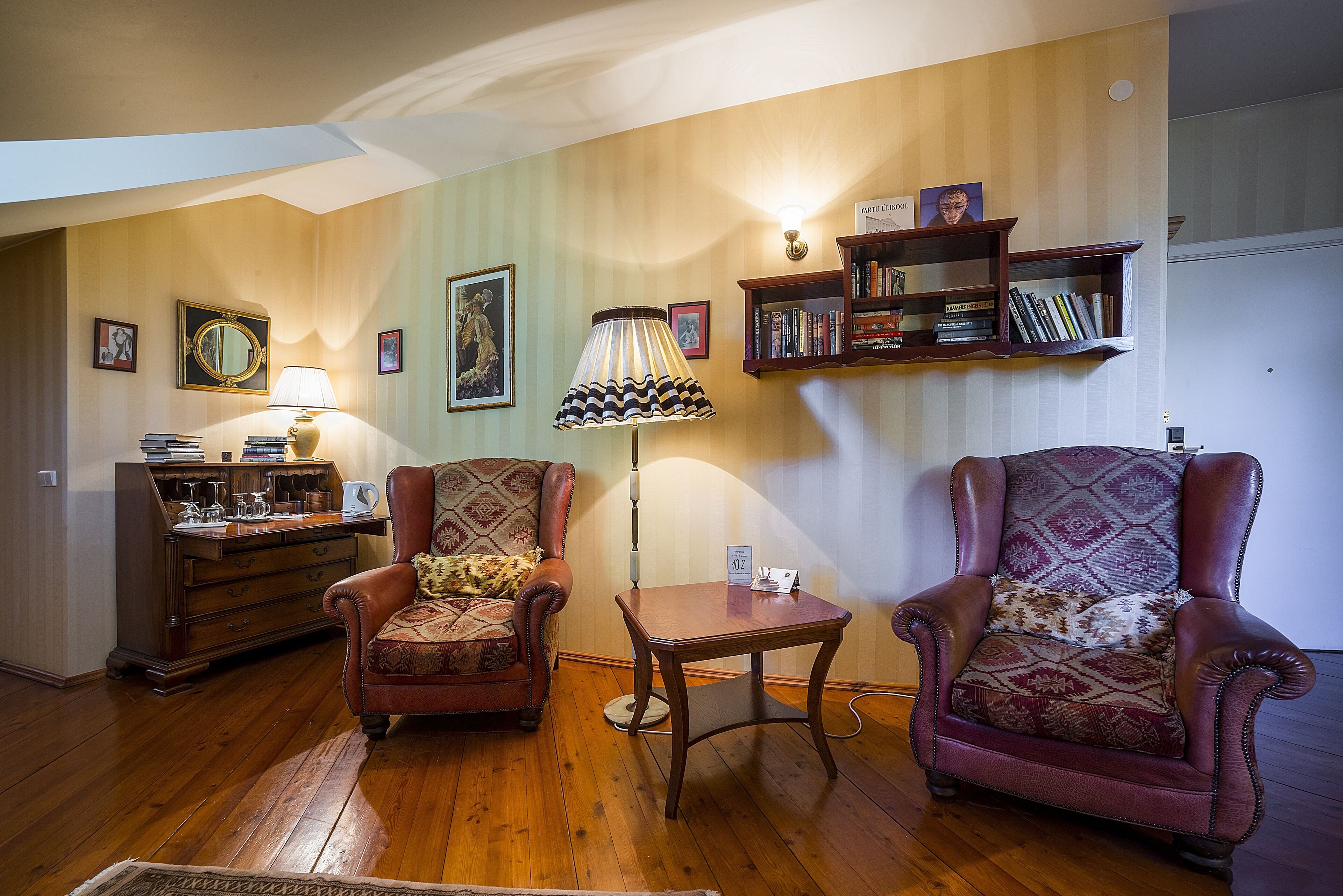 A living room with two armchairs, a wooden coffee table, a lamp, a bookshelf, and a mirror on the wall.