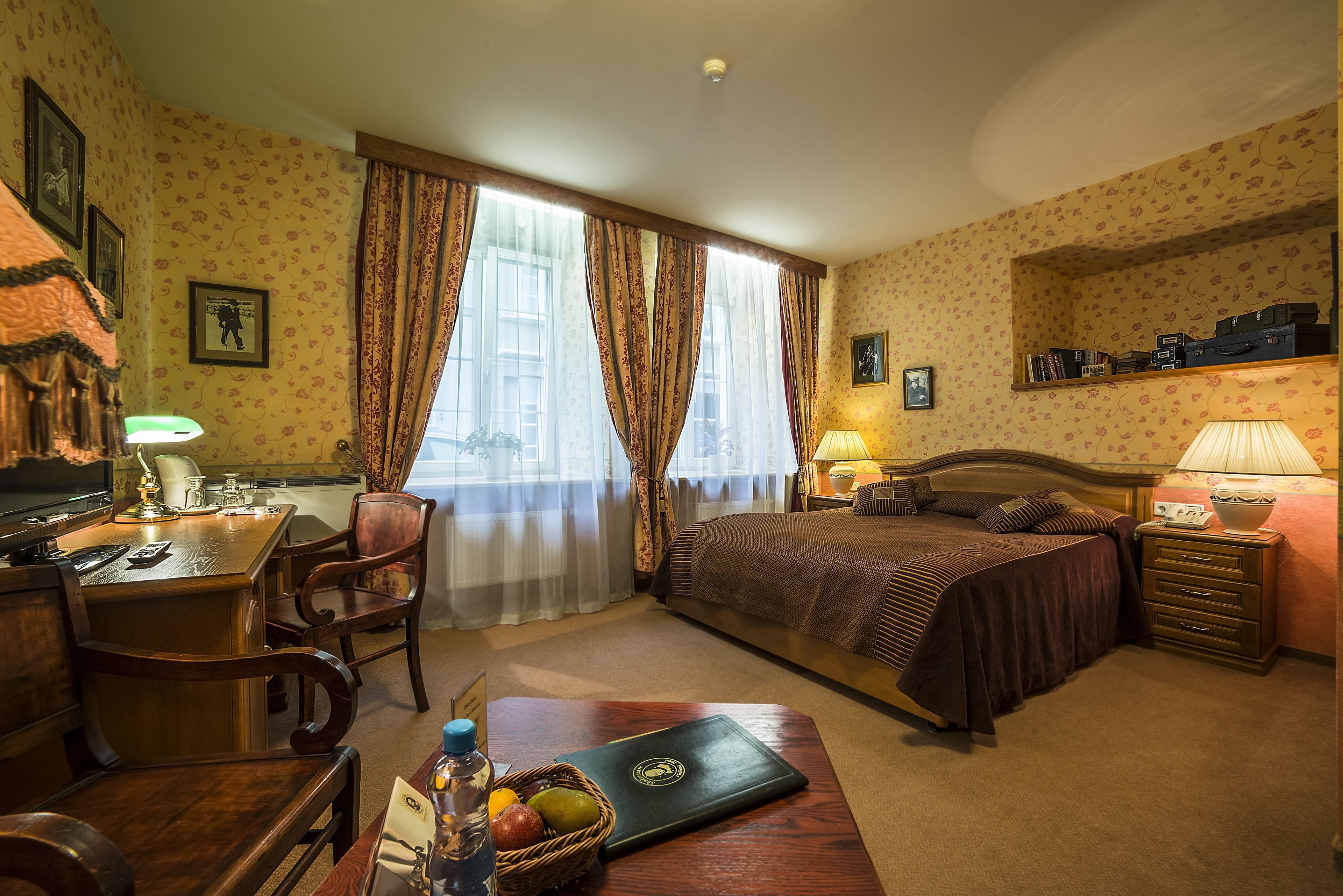 Quarto de hotel com cama, escrivaninha, cadeira e uma pequena mesa com cesta de frutas.