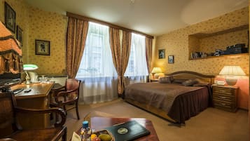 Quarto de hotel com cama, escrivaninha, cadeira e uma pequena mesa com cesta de frutas.