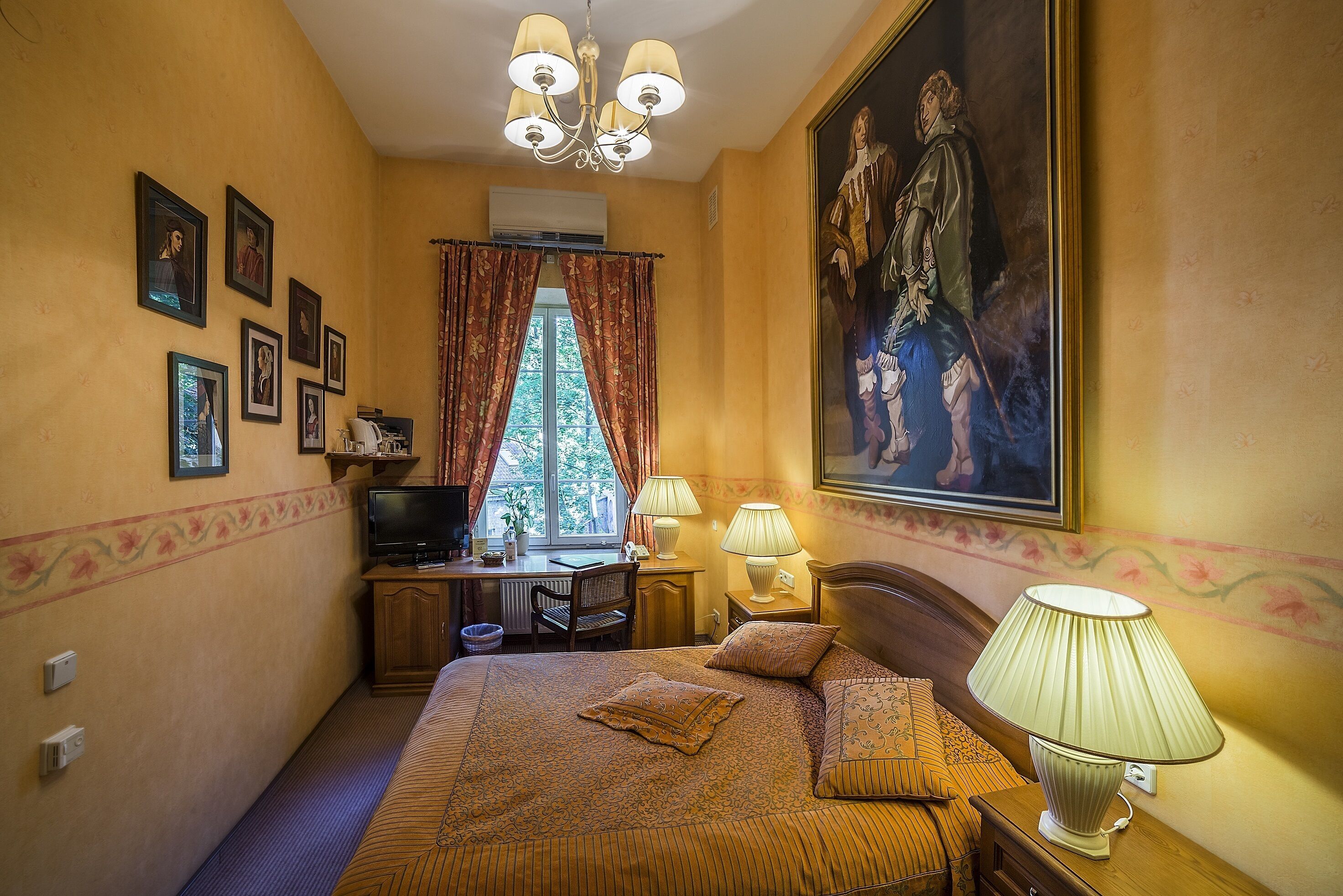 Una habitación de hotel con una cama, un escritorio, un televisor y un cuadro grande en la pared.