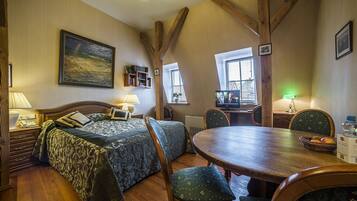 A cozy room with a bed, a dining table, and chairs. There is a window with blinds, a lamp, and a painting on the wall.
