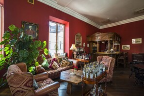 A room with a red wall, a large plant, a sofa, a table with bottles, and a bar area.