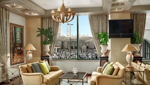 A spacious living room with a large window offering a view of a mosque and a crowd. Furnishings include a sofa set and a coffee table. - Madinah Hilton (Madinah)