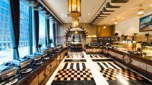 A hotel lobby with a checkered floor, a buffet area, and a view of the cityscape through large windows. - Madinah Hilton (Madinah)