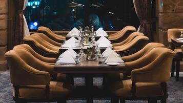 A formal dining room with a long table set for multiple guests, surrounded by upholstered chairs.
