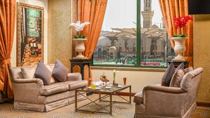 A luxurious room with a sofa, armchairs, a coffee table, and a view of a mosque through a window. - Madinah Hilton (Madinah)