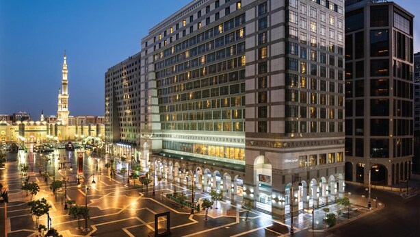 A modern hotel with a central courtyard, multiple floors, and a prominent minaret in the background. - Madinah Hilton (Madinah)