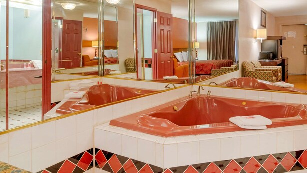 Un bany d'hotel amb un mirall gran, dues banyeres vermelles, un lavabo i una televisió.