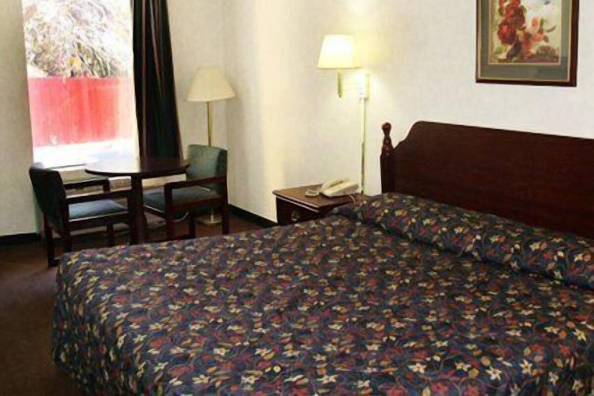 Hotellihuone, jossa on sänky, työpöytä, tuoli, lamppu ja taulu seinällä.
