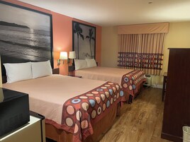 Habitación de hotel con dos camas, un escritorio, un televisor y un cuadro de una playa.