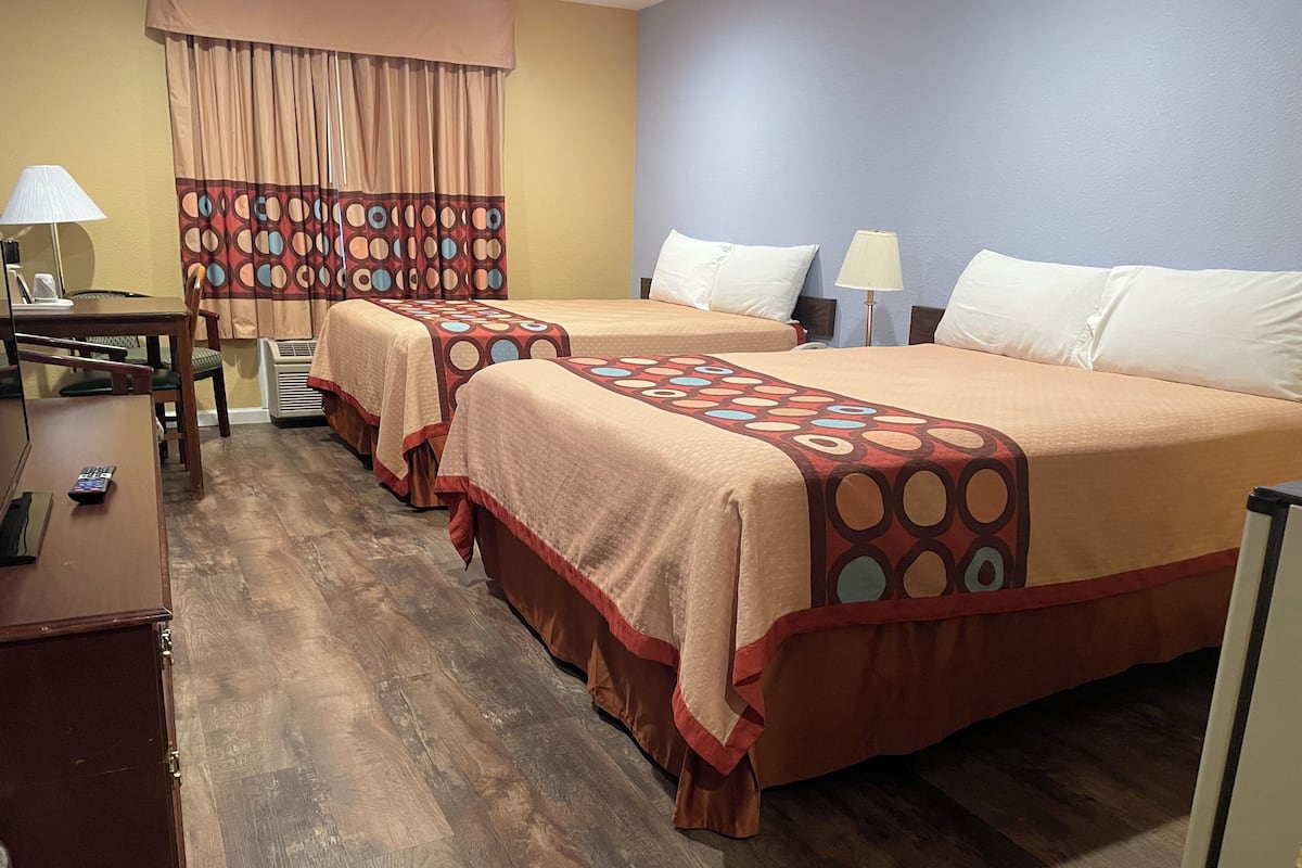 A hotel room with two beds, a desk, a chair, a lamp, and a window with curtains.