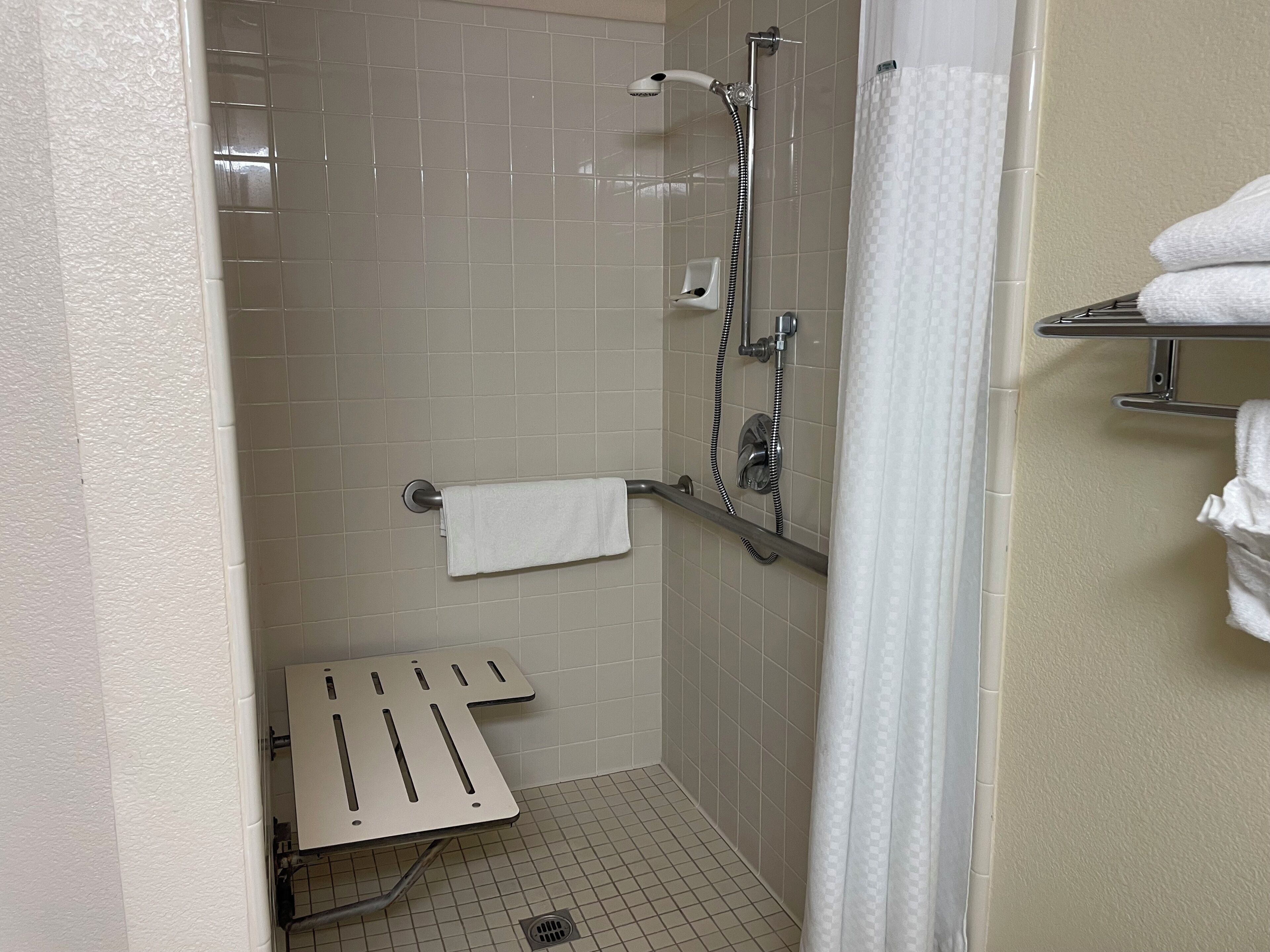 Un espacio de ducha pequeño con azulejos, un cabezal de ducha de mano, un perchero y un organizador para la ducha.