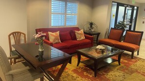 A hotel lobby with a red sofa, two armchairs, a glass coffee table, and a dining table with chairs. - Harvest Inn, Dixon/ UC Davis. (Dixon)