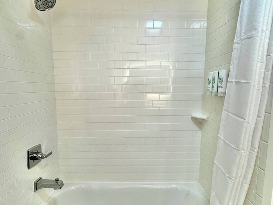 A modern bathroom with white tiled walls, a bathtub, a showerhead, and a shower curtain.