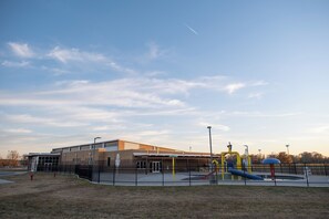 A playground with slides and swings, enclosed by a fence, and a building with a flat roof in the background. - Sleep Inn & Suites Searcy near University (Searcy)