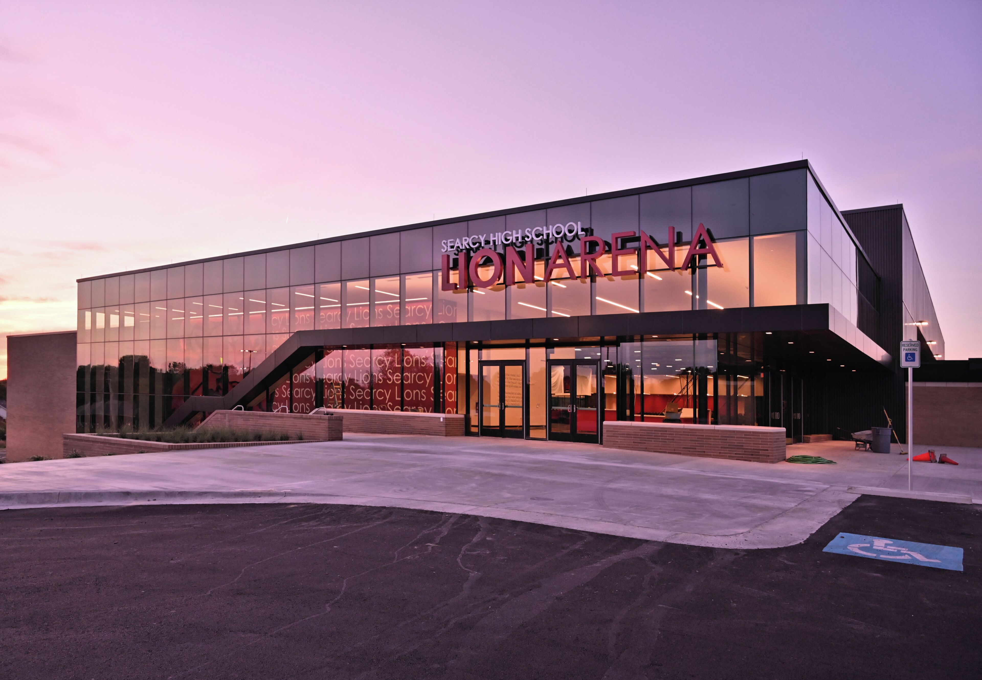 A modern building with a large glass facade, a prominent entrance, and a sign reading 'SEARCY HIGH SCHOOL LIONARENA'.
