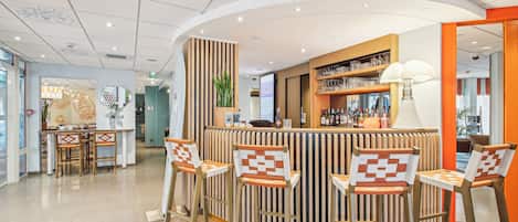 A modern bar area with a curved counter, wooden chairs with patterned cushions, and a variety of bottles and glasses on shelves.