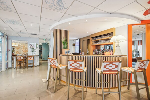 A modern bar area with a curved counter, wooden chairs with patterned cushions, and a variety of bottles and glasses on shelves.