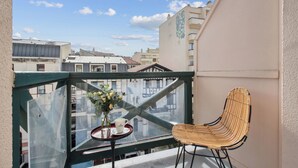 A balcony with a wicker chair, a small table with a vase and a cup, and a view of buildings. - Hôtel AKENA Biarritz - Grande plage (Biarritz)