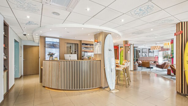 A modern hotel lobby with a reception desk, seating area, and a surfboard display. - Hôtel AKENA Biarritz - Grande plage (Biarritz)