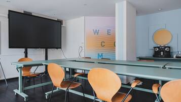 A conference room with a large table, chairs, a projector screen, a coffee machine, and a wall with a 'WELCOME' sign.
