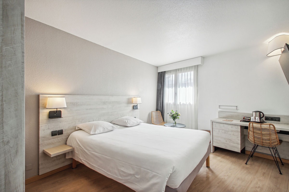 A modern hotel room with a large bed, bedside tables, a desk, and a chair.