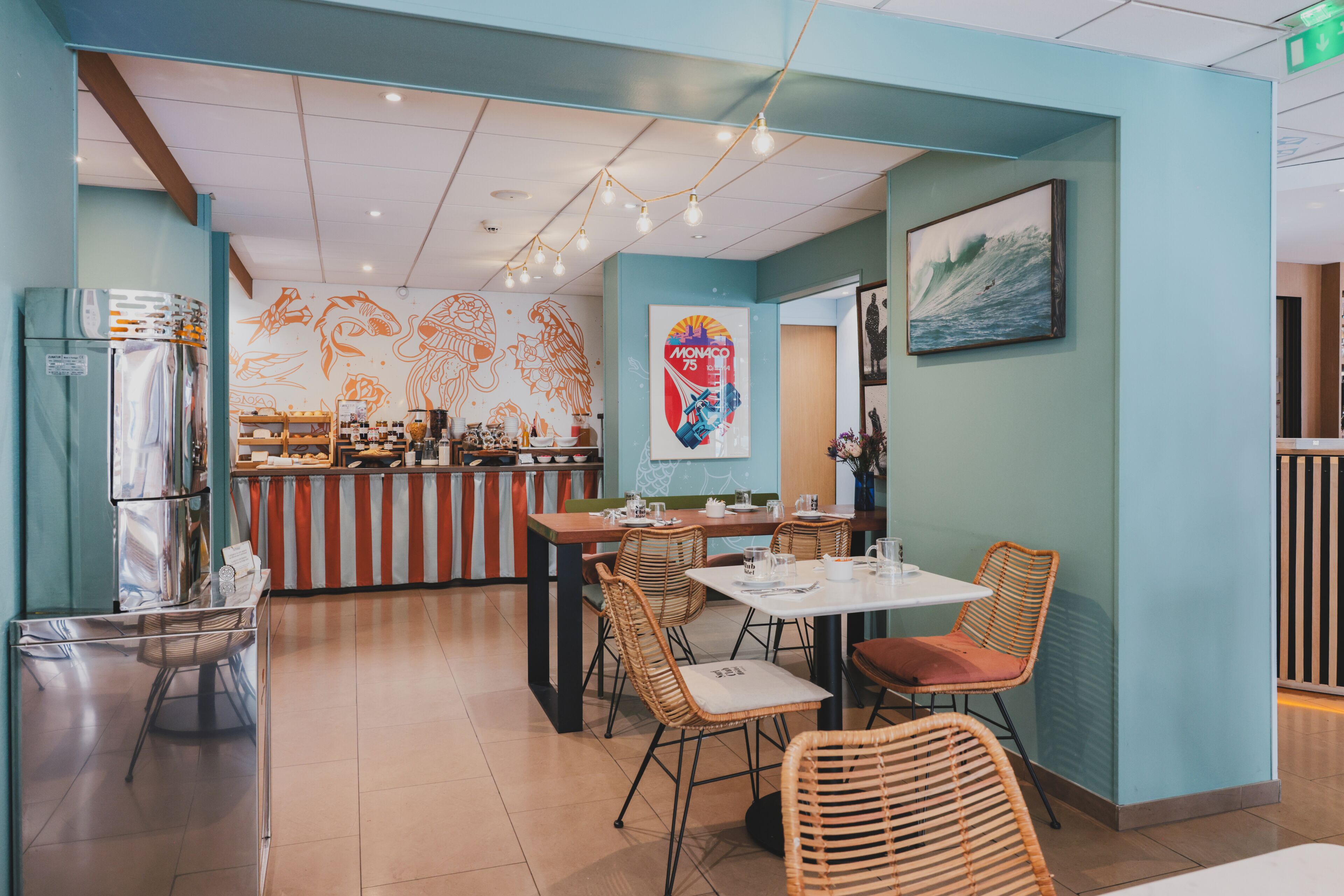 A restaurant with a counter, tables, wicker chairs, and a wall mural.