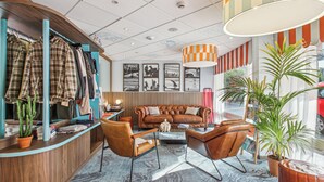 A modern interior with a wooden reception desk, a leather sofa, and a large window with a view. - Hôtel AKENA Biarritz - Grande plage (Biarritz)